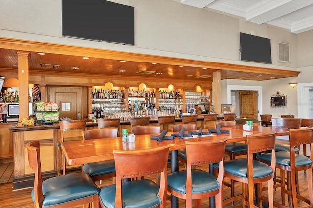 bar featuring wood finished floors, a community bar, a towering ceiling, visible vents, and beamed ceiling