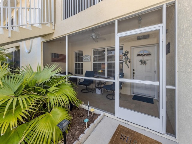 doorway to property featuring a ceiling fan, a balcony, and stucco siding