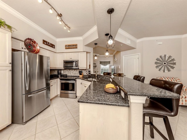 kitchen with a peninsula, a sink, appliances with stainless steel finishes, a kitchen bar, and decorative light fixtures