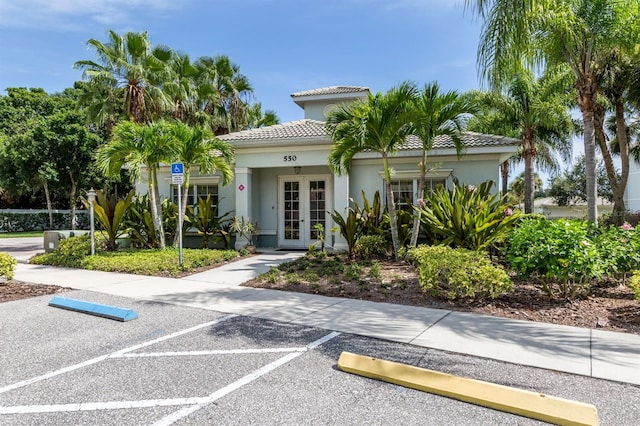 exterior space featuring a tile roof, uncovered parking, french doors, and stucco siding