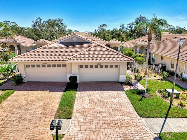 mediterranean / spanish house featuring a tiled roof, an attached garage, fence, decorative driveway, and stucco siding