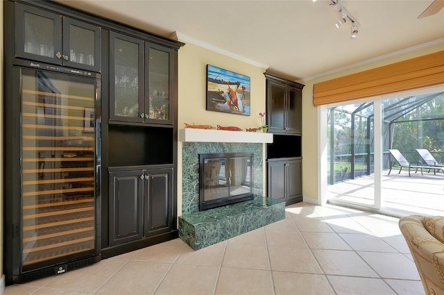 living area with light tile patterned floors, wine cooler, crown molding, a glass covered fireplace, and track lighting