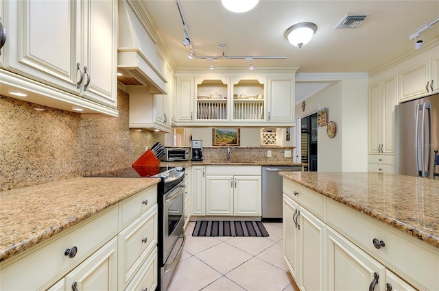 kitchen with light tile patterned floors, light stone counters, stainless steel appliances, visible vents, and glass insert cabinets