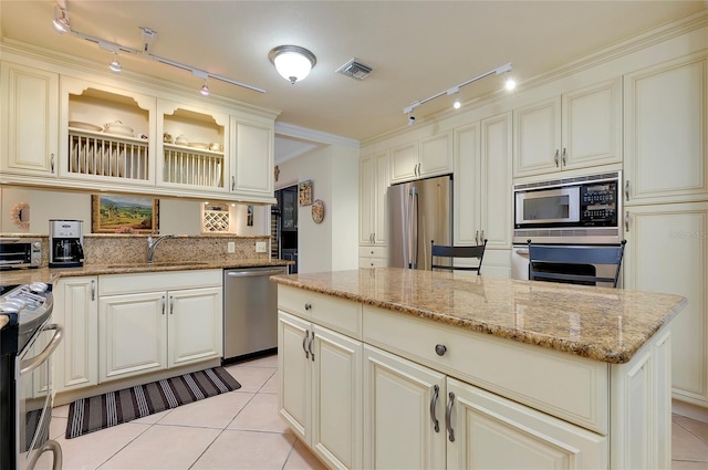 kitchen featuring light stone counters, a center island, stainless steel appliances, glass insert cabinets, and a sink