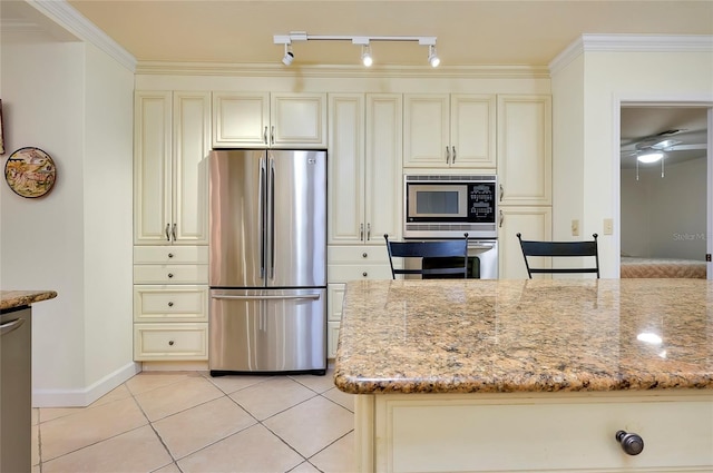 kitchen with stainless steel appliances, cream cabinetry, light stone counters, and light tile patterned floors