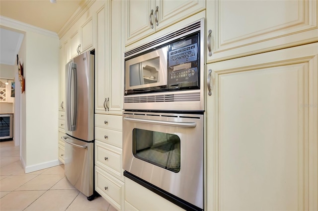 kitchen featuring light tile patterned floors, cream cabinets, baseboards, ornamental molding, and appliances with stainless steel finishes