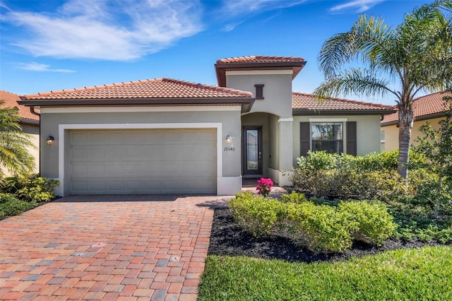 mediterranean / spanish home featuring a garage, decorative driveway, a tiled roof, and stucco siding