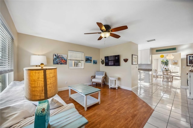 living area featuring light tile patterned floors, visible vents, baseboards, and a ceiling fan