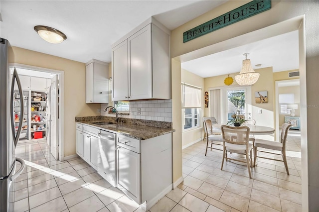 kitchen featuring light tile patterned floors, decorative backsplash, dark stone counters, stainless steel appliances, and a sink