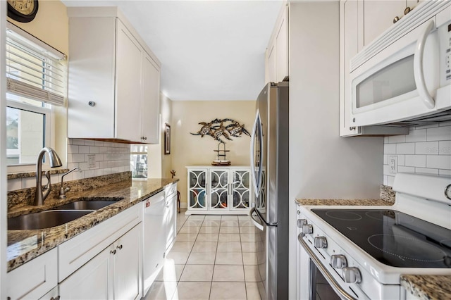 kitchen featuring white appliances, light tile patterned flooring, a sink, and white cabinets