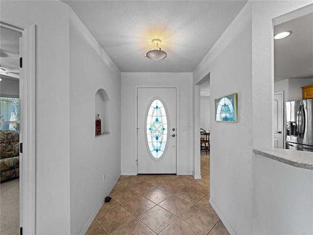 entrance foyer featuring a textured ceiling, light tile patterned flooring, baseboards, and a healthy amount of sunlight