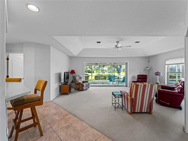 carpeted living area featuring plenty of natural light, a tray ceiling, a ceiling fan, and tile patterned floors