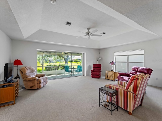 living room featuring carpet, visible vents, a raised ceiling, and a textured ceiling