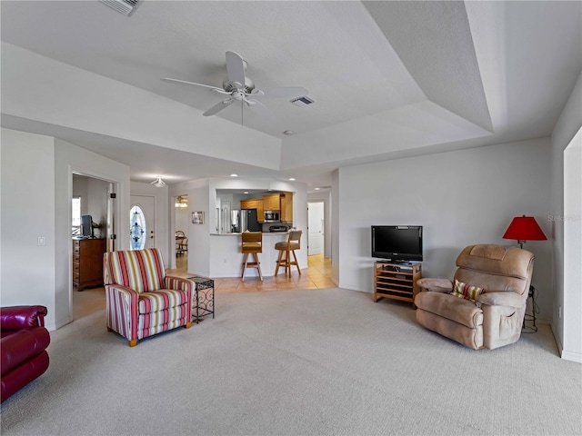 living room with light carpet, baseboards, visible vents, ceiling fan, and a tray ceiling