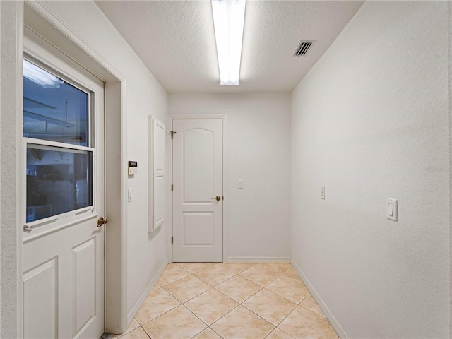 entryway featuring a textured ceiling, light tile patterned floors, visible vents, and baseboards