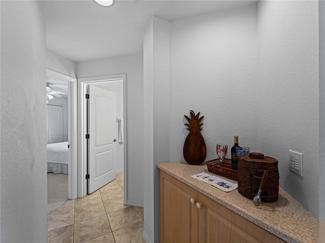 corridor featuring a textured wall, baseboards, and light tile patterned floors