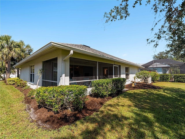 rear view of house featuring a sunroom, stucco siding, and a yard