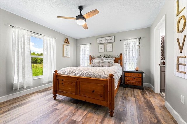 bedroom featuring dark wood-type flooring, a textured ceiling, baseboards, and a ceiling fan