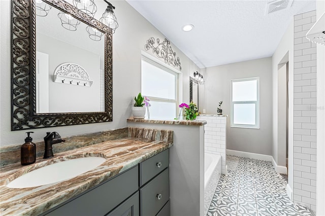 bathroom featuring visible vents, a bathing tub, vanity, a textured ceiling, and baseboards