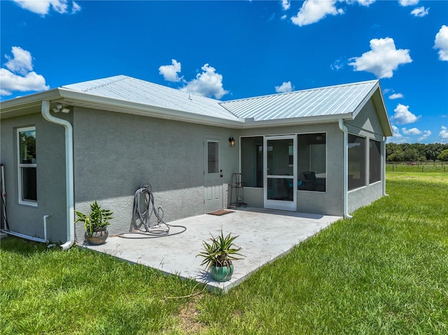 back of property featuring a yard, a patio, stucco siding, a sunroom, and metal roof