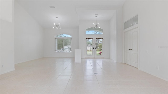 interior space with light tile patterned floors, a notable chandelier, a towering ceiling, baseboards, and french doors