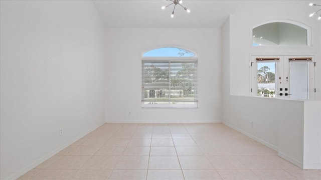 tiled empty room with a chandelier, vaulted ceiling, and baseboards