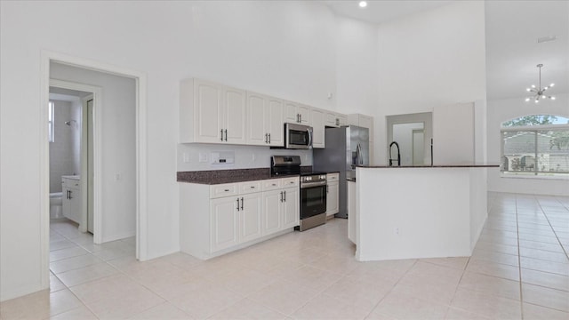 kitchen with light tile patterned floors, appliances with stainless steel finishes, white cabinets, and a notable chandelier