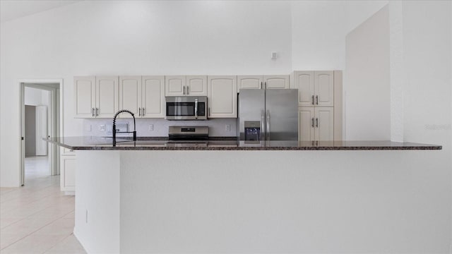 kitchen featuring light tile patterned floors, a high ceiling, stainless steel appliances, and dark stone countertops