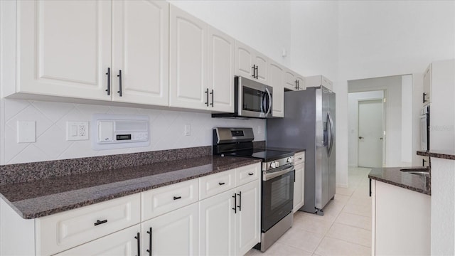 kitchen with light tile patterned floors, appliances with stainless steel finishes, white cabinets, and dark stone countertops