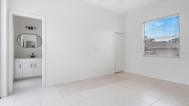 empty room featuring light tile patterned floors, ceiling fan, baseboards, and a sink