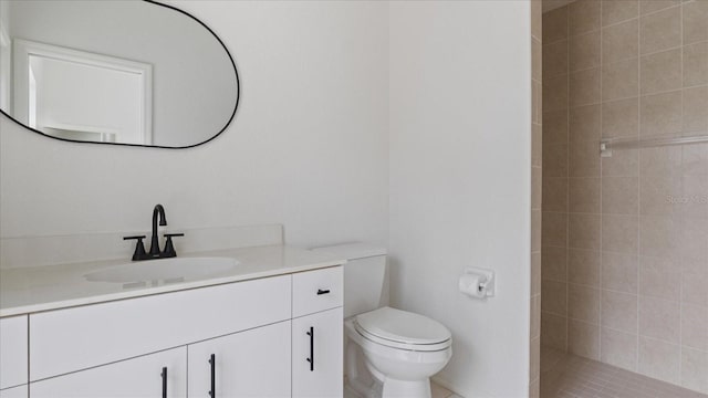 full bathroom with toilet, a tile shower, and vanity