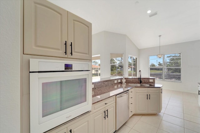 kitchen featuring lofted ceiling, light stone counters, a sink, white oven, and stainless steel dishwasher