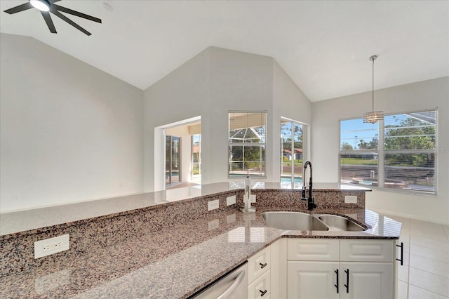 kitchen featuring lofted ceiling, a sink, white cabinetry, dark stone countertops, and decorative light fixtures