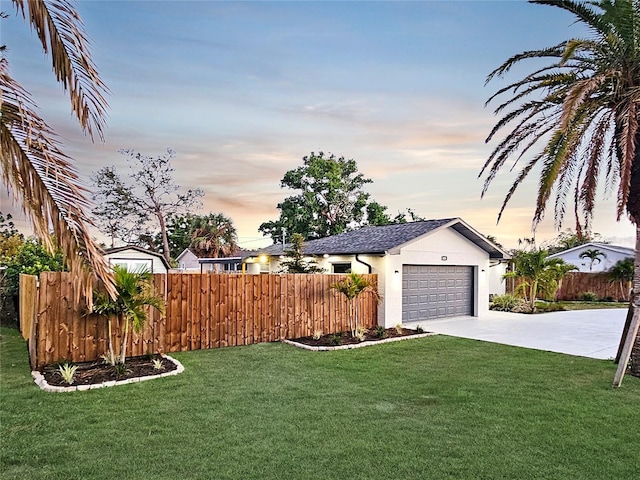 yard at dusk with a garage, concrete driveway, and fence