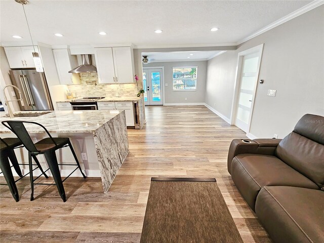 kitchen with open floor plan, wall chimney exhaust hood, white cabinets, and light stone countertops