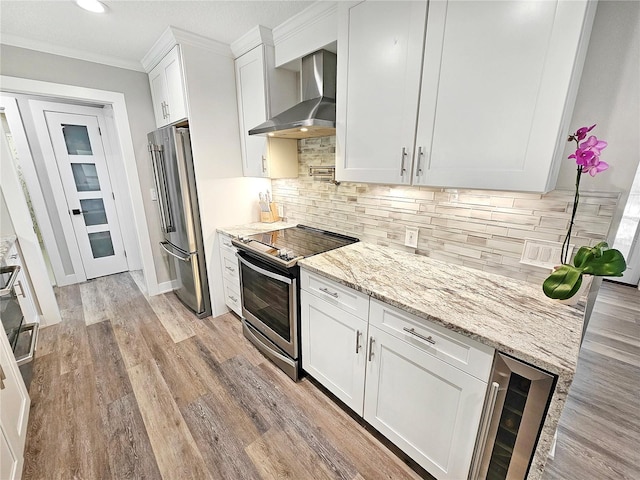 kitchen with appliances with stainless steel finishes, wine cooler, white cabinets, and wall chimney range hood