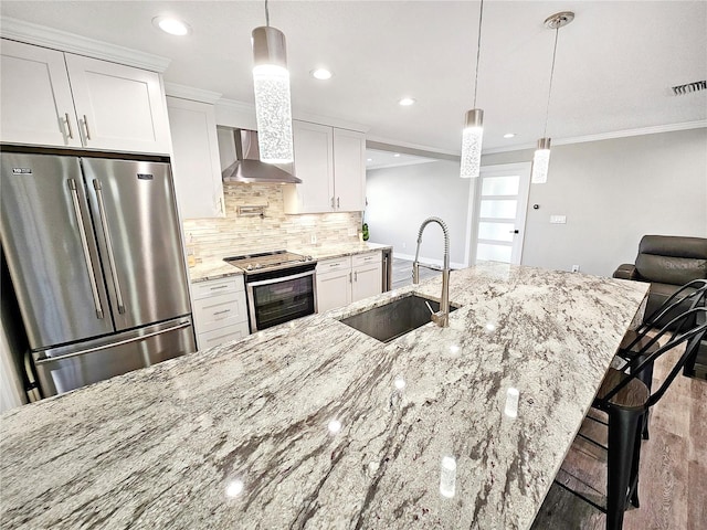 kitchen featuring white cabinets, wall chimney exhaust hood, a breakfast bar area, appliances with stainless steel finishes, and a sink