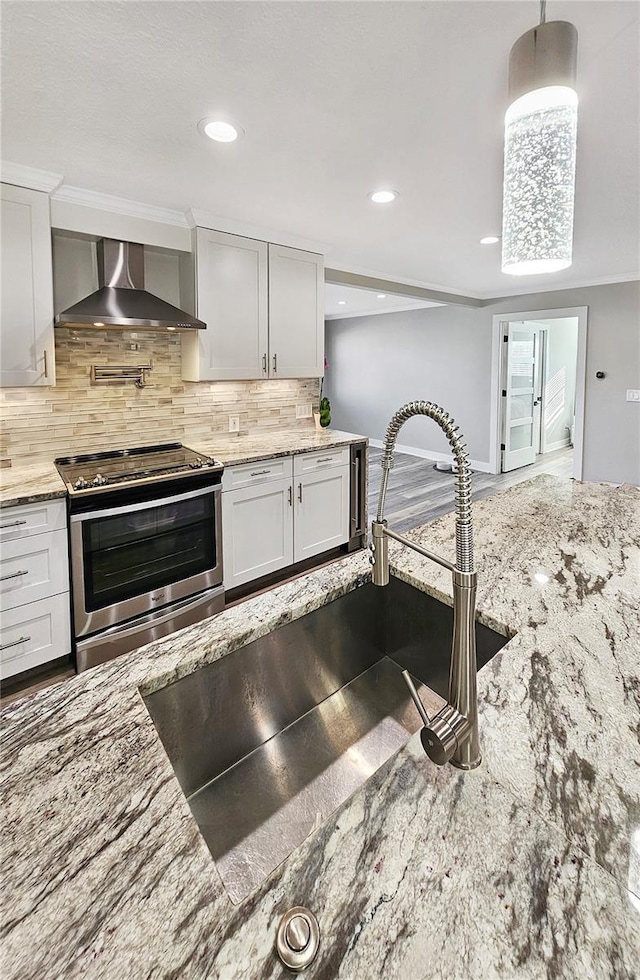 kitchen featuring a sink, backsplash, light stone countertops, stainless steel electric range oven, and wall chimney exhaust hood