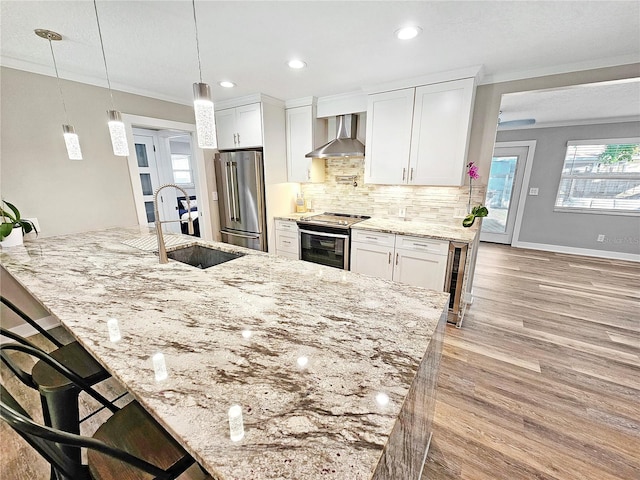 kitchen with pendant lighting, appliances with stainless steel finishes, white cabinets, a sink, and wall chimney exhaust hood