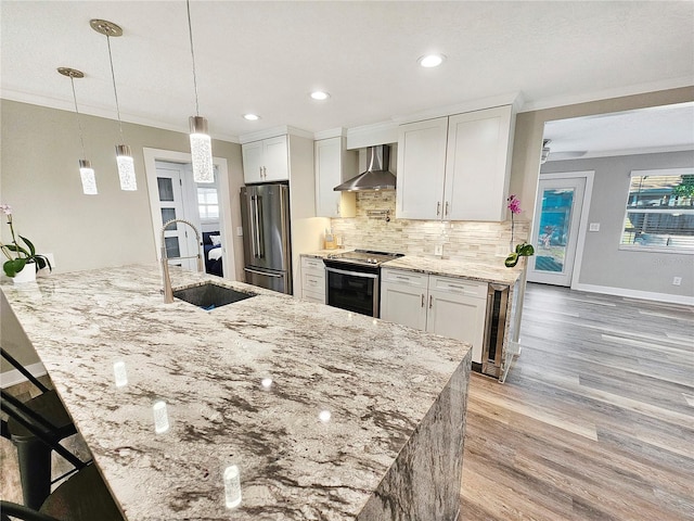 kitchen featuring white cabinets, wall chimney range hood, stainless steel appliances, and a sink