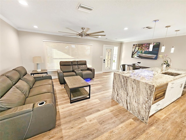 living area with ornamental molding, light wood-style flooring, visible vents, and recessed lighting