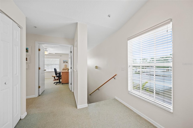 hall featuring baseboards, light colored carpet, and an upstairs landing