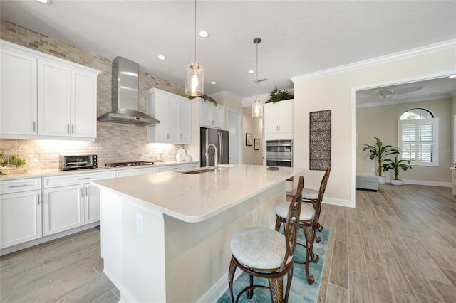 kitchen featuring light countertops, wall chimney range hood, an island with sink, and white cabinetry