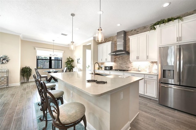 kitchen with wall chimney exhaust hood, white cabinets, a sink, and stainless steel fridge with ice dispenser