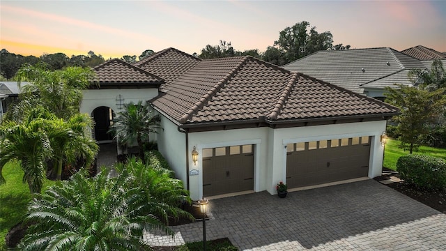 mediterranean / spanish home with a garage, a tile roof, decorative driveway, and stucco siding