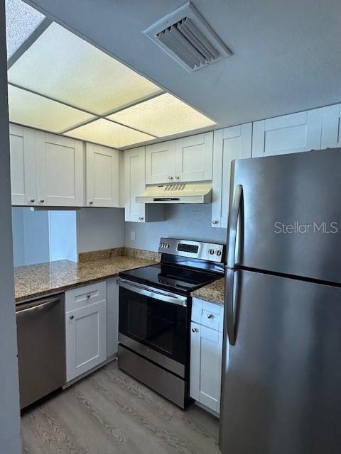 kitchen with light wood finished floors, visible vents, appliances with stainless steel finishes, under cabinet range hood, and white cabinetry