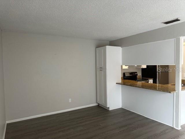 kitchen featuring refrigerator, dark wood-style flooring, stainless steel electric stove, visible vents, and white cabinetry