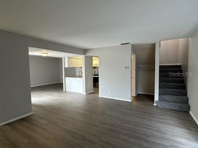 unfurnished living room featuring dark wood-type flooring, visible vents, stairway, and baseboards