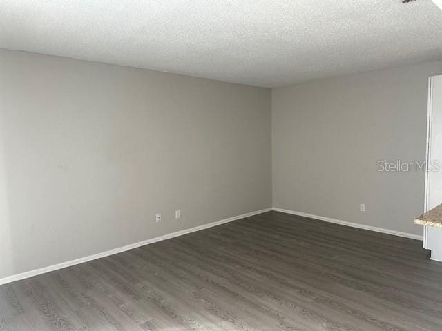 spare room featuring a textured ceiling, baseboards, and dark wood-type flooring