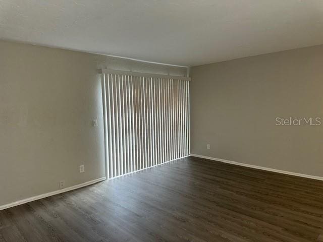 spare room featuring baseboards and dark wood-style flooring